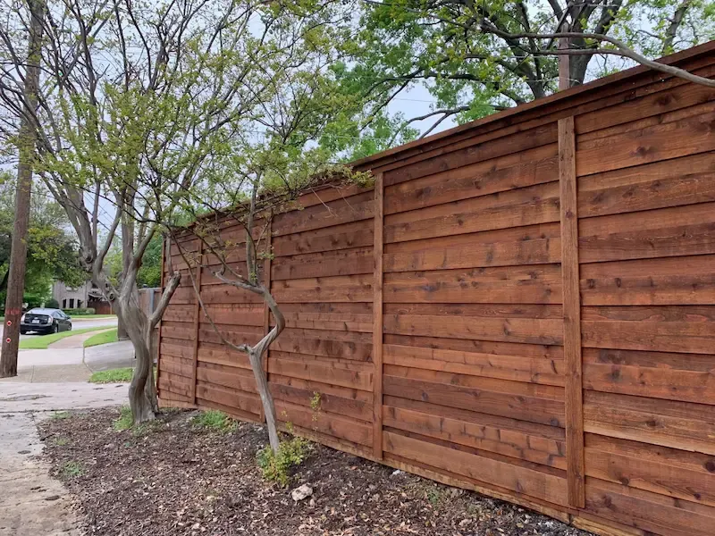 Horizontal cedar privacy fence with stained boards along a tree-lined yard