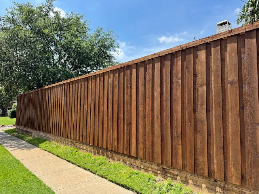 Wood privacy fence with a flat top cap beside a sidewalk and lawn.